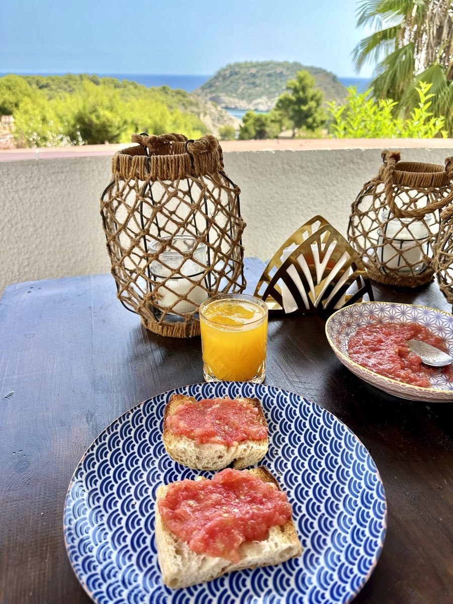 Desayuno de pan con tomate y zumo en la terraza, con la isla al fondo